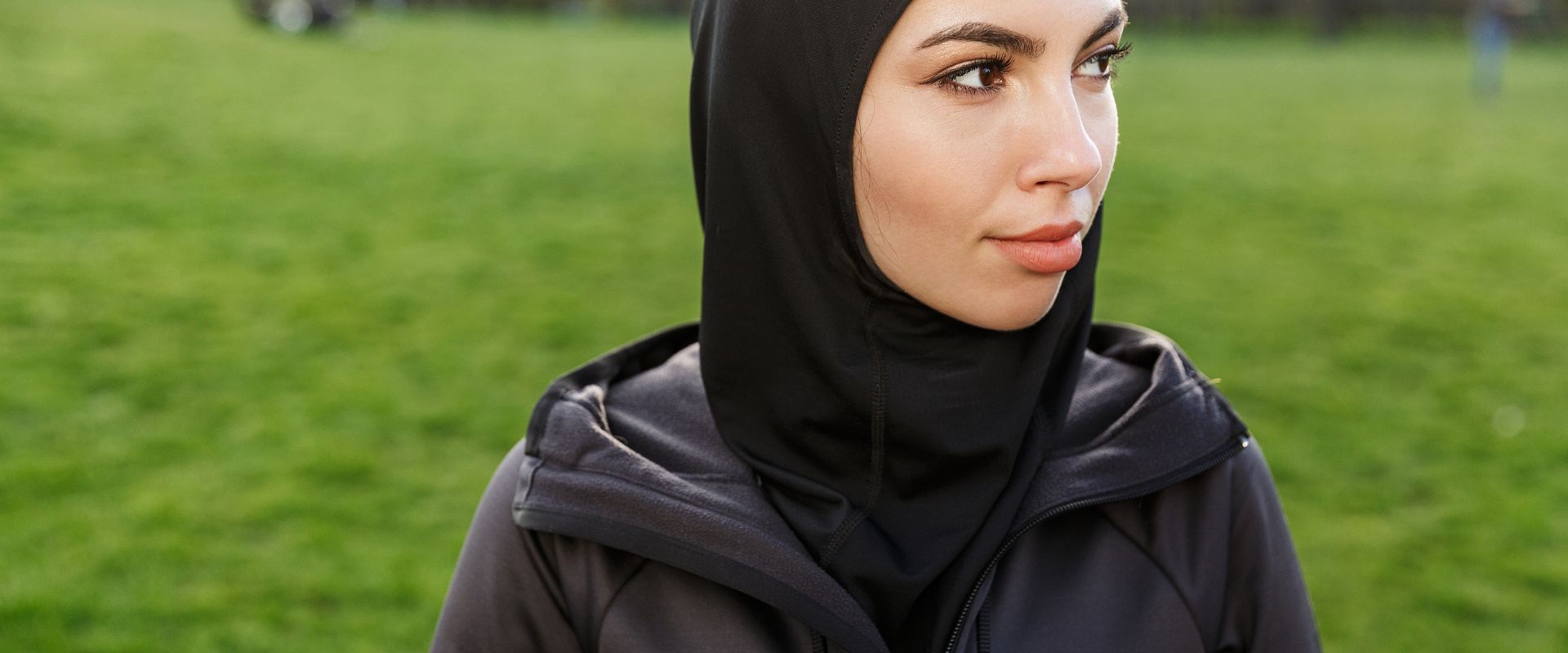 A woman goes for a run in a field with a black fitness hoodie on.